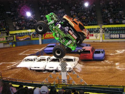1996 Ford Bronco - A monster truck performs a stunt, leaping over several destroyed cars during an event.