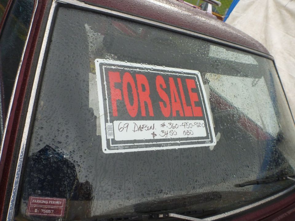 Red 'For Sale' sign on a wet windshield reads '69 Datsun' and a phone number
