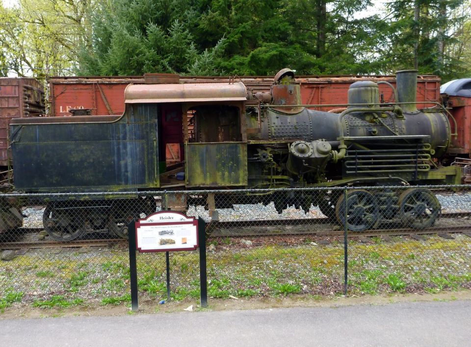 Old steam locomotive with weathered paint, next to a red train car