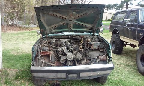1990 Ford Bronco - The engine bay of a green truck is exposed with the hood open, while a black Bronco sits in the background.