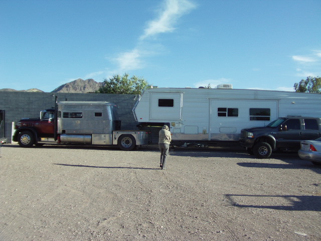 Custom truck towing a large trailer, with a pickup truck parked nearby