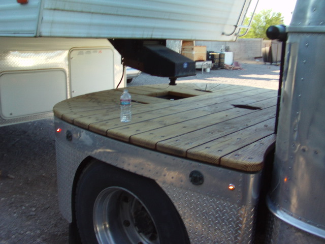 Truck bed with wooden deck, fifth wheel hitch, and trailer landing gear. Diamond plate fender