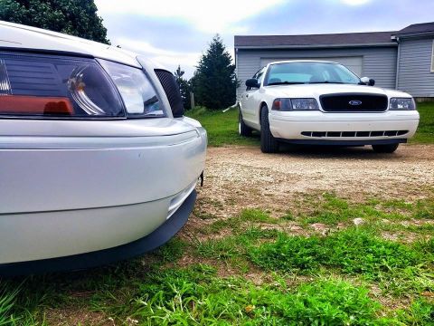 2000 Mercury Grand Marquis - Two white Ford Crown Victorias are parked in front of a garage on a gravel driveway.
