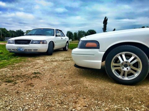 2000 Mercury Grand Marquis - Two white sedans are parked on a gravel road under a cloudy sky.