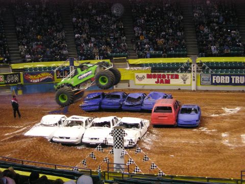 1996 Ford Bronco - A monster truck performs a jump over a line of wrecked cars during an indoor event.