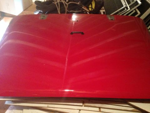 1979 Ford Bronco - A red vehicle hood is shown, possibly for a truck or SUV, with a central handle and mounting hardware visible.