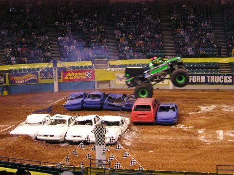1996 Ford Bronco - A monster truck soars over a pile of wrecked cars during a show.
