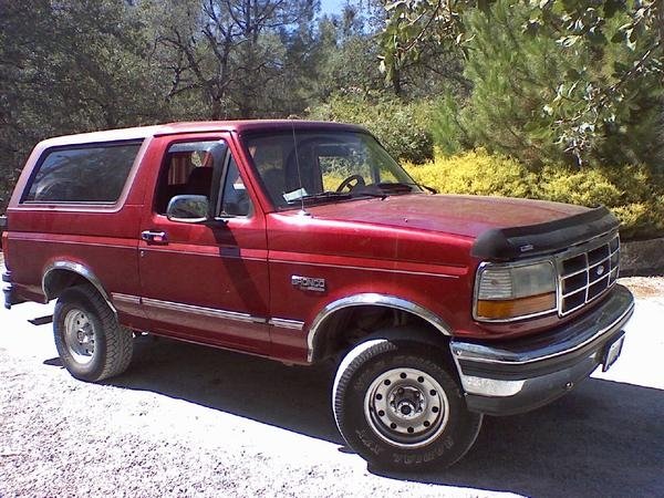 Red Ford Bronco parked outside with trees and bushes in the background