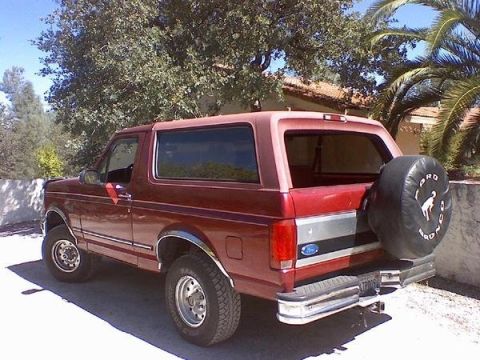 1995 Ford Bronco - Rear view of a red Ford Bronco parked outdoors with trees and a house in the background.