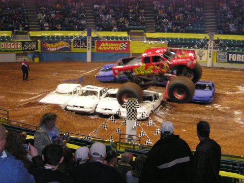 1996 Ford Bronco - A monster truck event shows a large truck crushing several cars in an indoor arena with spectators.