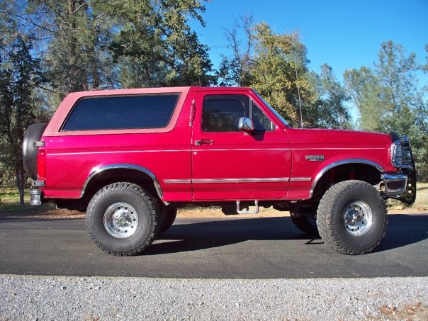 Red Ford Bronco with aftermarket wheels and tires, lifted suspension, and a tan removable top