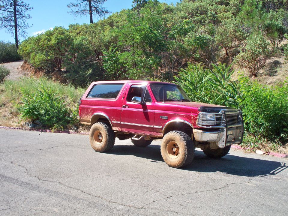Red 1995 Ford Bronco with lifted suspension and aftermarket grille guard parked on a dirt road