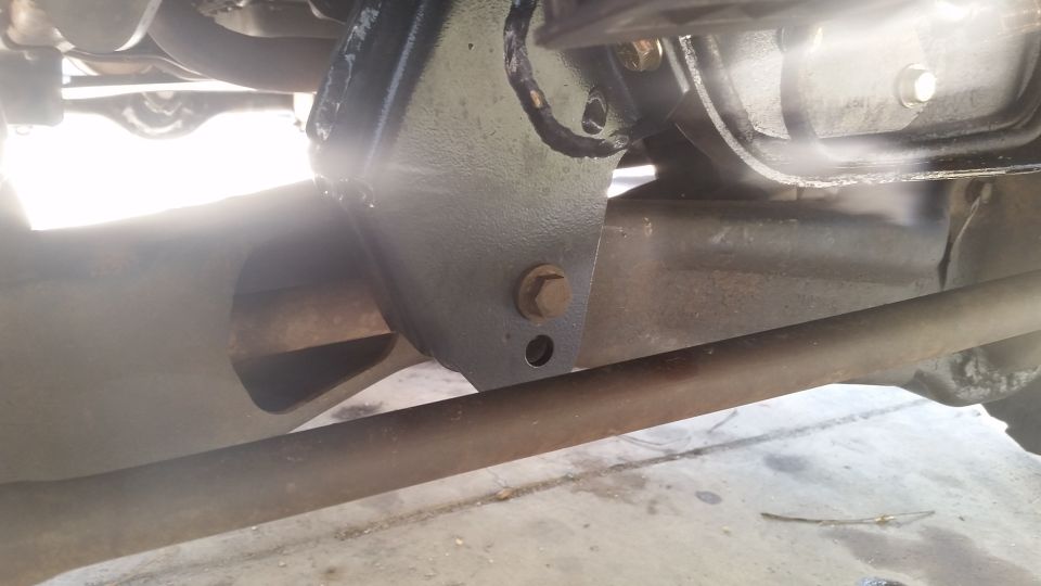 close-up of a metal bracket bolted to a vehicle's frame, with a rusty bar below it