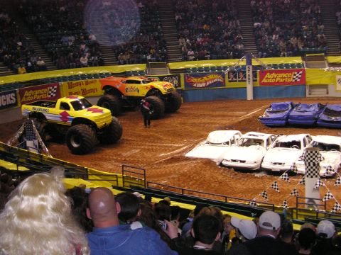 1996 Ford Bronco - Monster trucks are set up in an arena, ready to crush cars in front of a crowd.