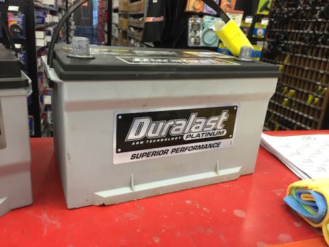 1989 Ford Bronco - A Duralast Platinum AGM battery is displayed on a red surface in an auto parts store.