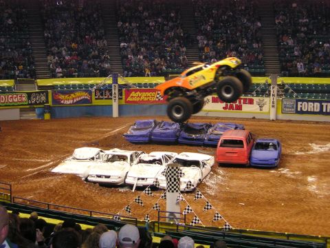 1996 Ford Bronco - A monster truck soars through the air over a pile of crushed cars during a Monster Jam event.