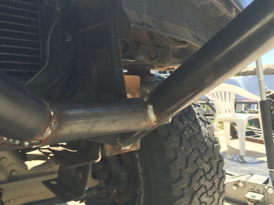 Underside view of welded exhaust pipe near radiator and off-road tire