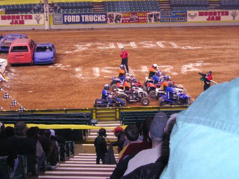 1996 Ford Bronco - Monster Jam event features ATVs lined up on the dirt track with cars in the background.