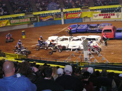 1996 Ford Bronco - ATVs navigate a dirt arena filled with wrecked cars during a Monster Jam event.