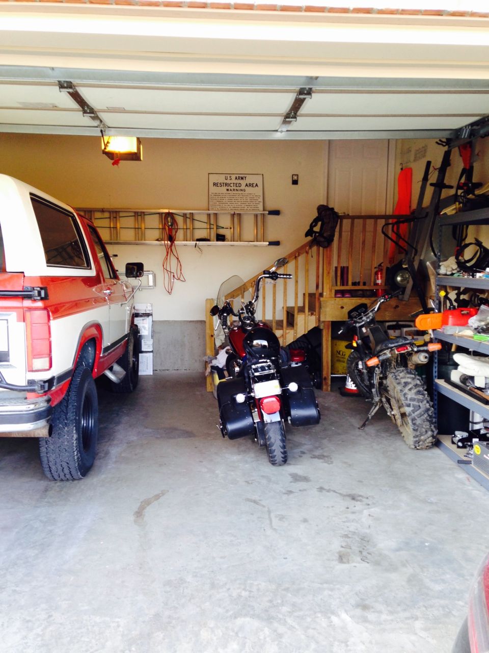 red and white SUV parked next to two motorcycles in a garage. U.S. Army Restricted Area sign on wall