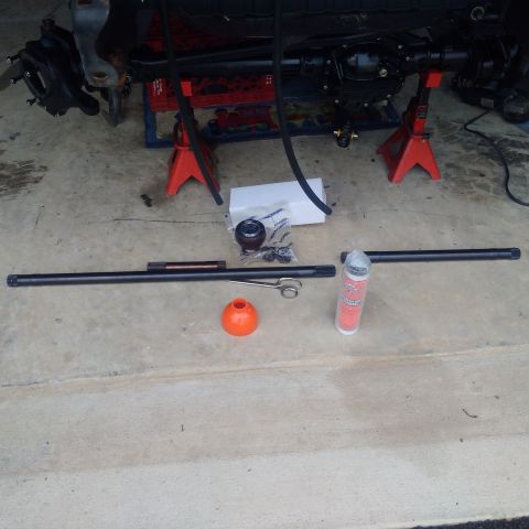 1978 Ford Bronco - Various suspension components, including tie rods and a ball joint, are arranged on the ground next to a vehicle's axle assembly.