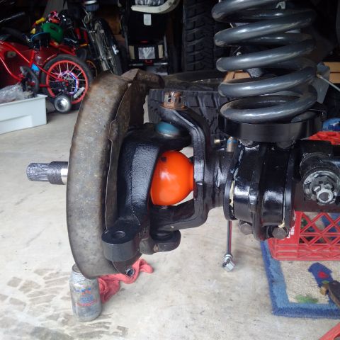 1978 Ford Bronco - Close-up view of a vehicle's suspension component, an orange ball joint and a large coil spring.