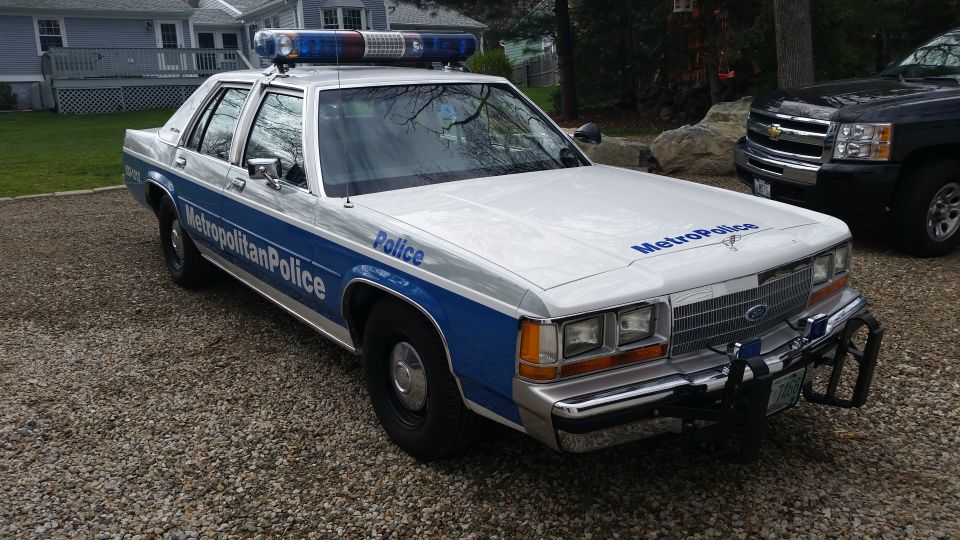 1991 Ford Crown Victoria LTD police car with Metropolitan Police markings, parked on gravel next to a black SUV