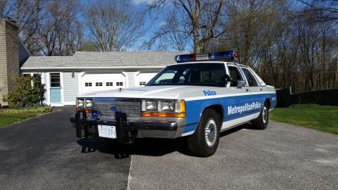 1991 Ford LTD Crown Victoria - Police car with 'Metropolitan Police' text on the side is parked in front of a garage.