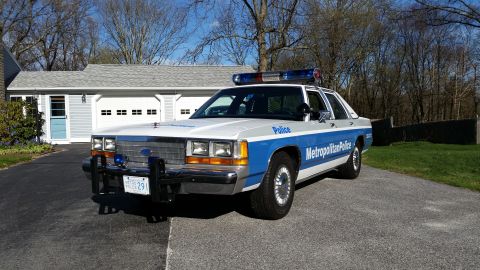 1991 Ford LTD Crown Victoria - A police car is parked in a driveway in front of a house and garage.