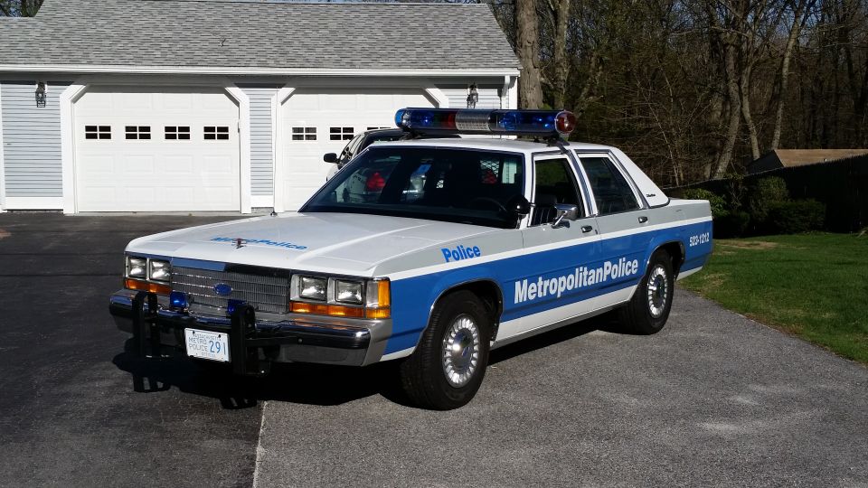 White and blue 1991 Ford Crown Victoria LTD police car with light bar, parked in driveway