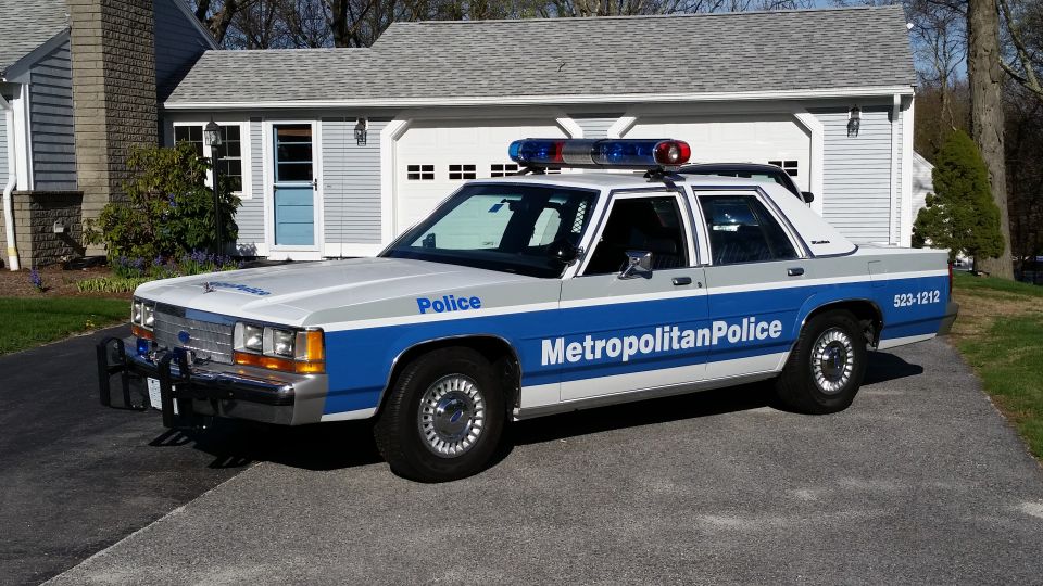 White and blue police car with light bar, parked in driveway
