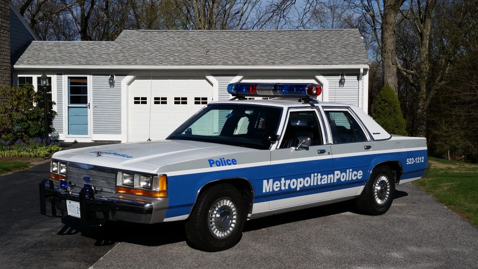 Police car parked in driveway in front of a garage. It has blue and red lights on top and 'Metropolitan Police' written on the side