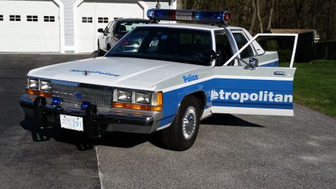 1991 Ford LTD Crown Victoria - A police car with 'Metropolitan Police' text is parked in front of a garage.