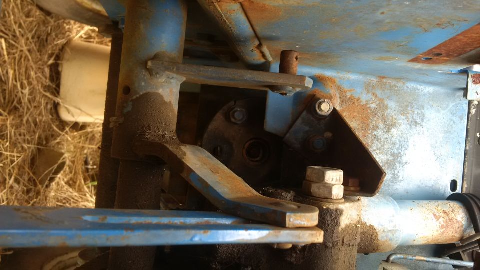 Blue painted metal tractor component with rust and grease, showing bolts and linkages