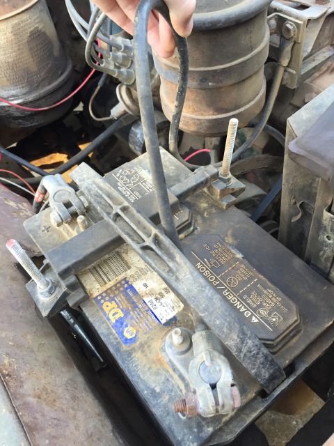 1946 Jeep CJ5 - Close-up of a car battery and surrounding engine parts, with a hand holding a cable.