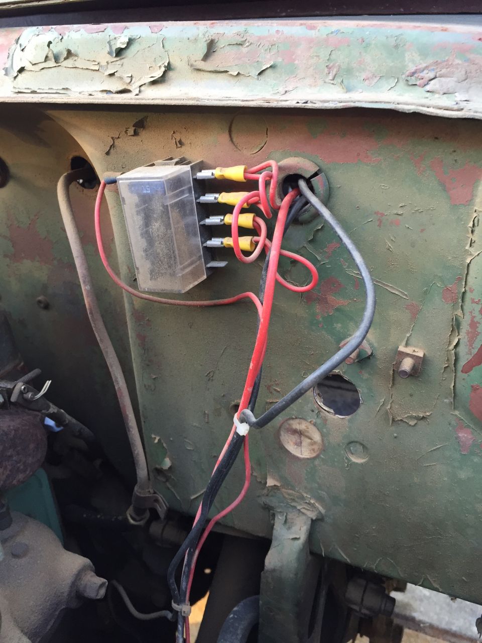 Fuse box with red and black wires attached to a green, weathered metal panel