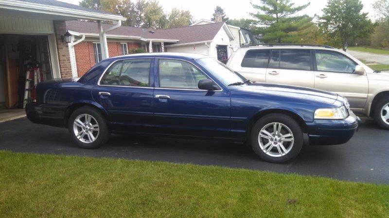 Blue 2006 Ford Crown Victoria parked next to a tan SUV in a driveway