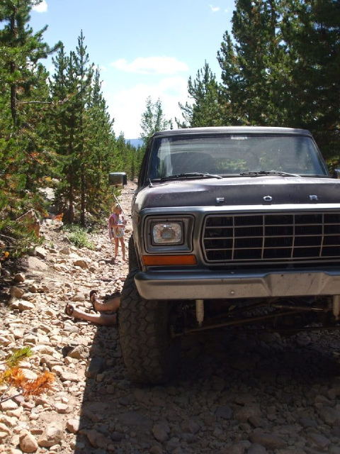 1979 Ford Bronco - Front view of a 1979 Ford Bronco on a rocky, wooded trail with two people visible.