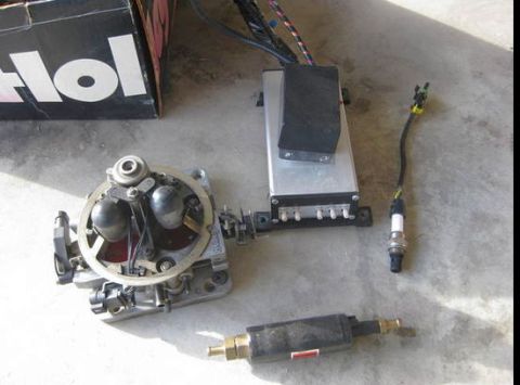 1979 Ford Bronco - Carburetor, ignition control module, and a spark plug are laid out on a concrete surface.