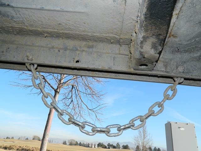 Underside of a vehicle with a chain attached, showing a tree and sky in the background