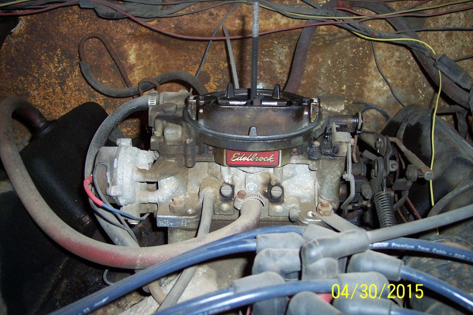 Edelbrock carburetor with red label, mounted in engine bay with wiring and hoses