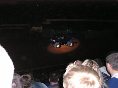 1996 Ford Bronco - A monster truck is illuminated by a spotlight in a dark arena, viewed from an audience perspective.