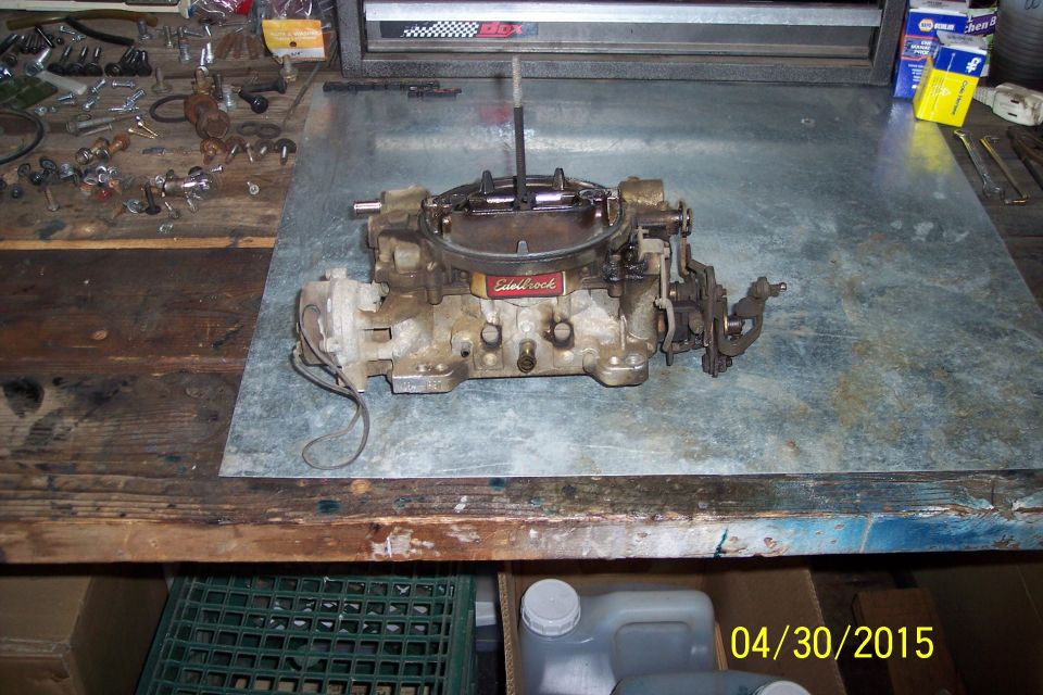 Edelbrock carburetor with red label on metal workbench, tools scattered nearby