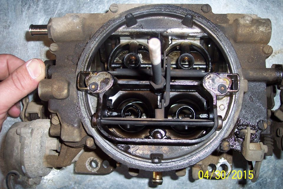 Close-up of a dirty carburetor with a hand on the side
