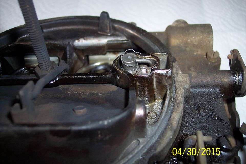 Carburetor with visible oil and grime, showing a spring-loaded mechanism and a wire