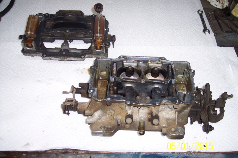 Disassembled carburetor with two main sections on a white surface. A wrench is visible in the background