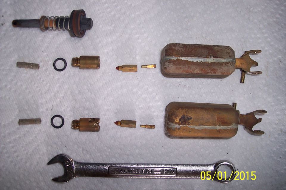Carburetor float bowls, jets, O-rings, and a spring-loaded plunger disassembled, with a 15/16 inch wrench