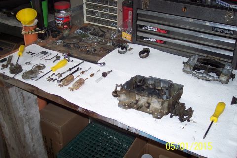 1973 Ford F-250 - Tools and disassembled carburetor parts are spread out on a workbench for a rebuild project.