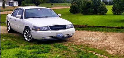 2000 Mercury Grand Marquis - A white sedan is parked on a gravel driveway next to a grassy area with trees.