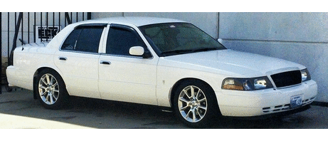 2000 Mercury Grand Marquis - A white 2000 Mercury Grand Marquis sedan is viewed from a three-quarter front angle, parked in front of a building.